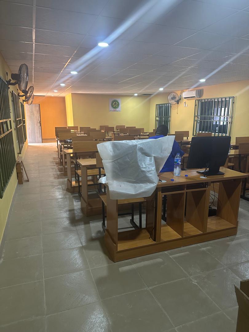 Interior of the completed ICT Centre with rows of wooden desks, a computer monitor, wall-mounted air conditioner and fans