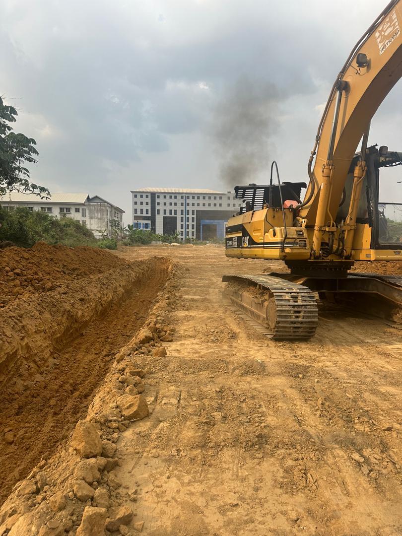 Excavator digging the road trench during earthworks, with a multi-storey building in the background