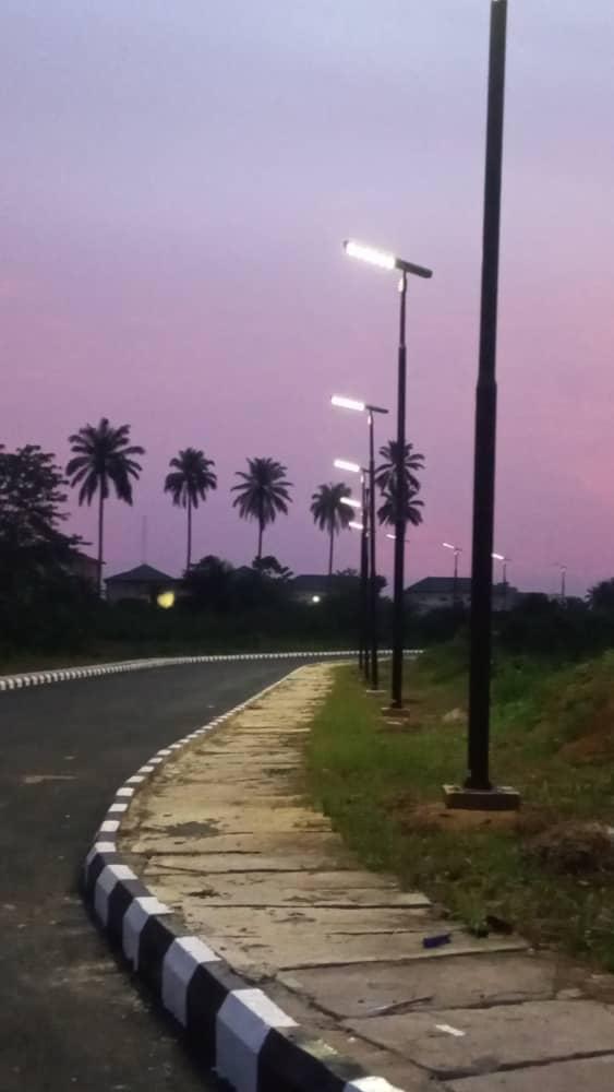 Row of illuminated streetlights along the finished road's paved sidewalk at dusk